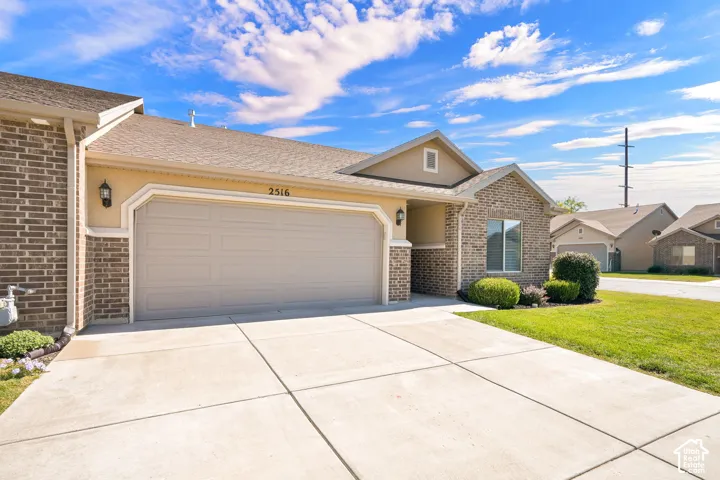 Brick and stucco exterior, attached two-car garage, concrete driveway, and front lawn