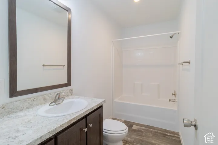 Vanity with a single basin sink, white bathtub with a shower, wood-finish flooring, and a framed mirror