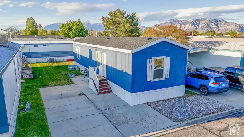 Blue and white siding, white window trim, front entry with steps, paved driveway, and mountain backdrop