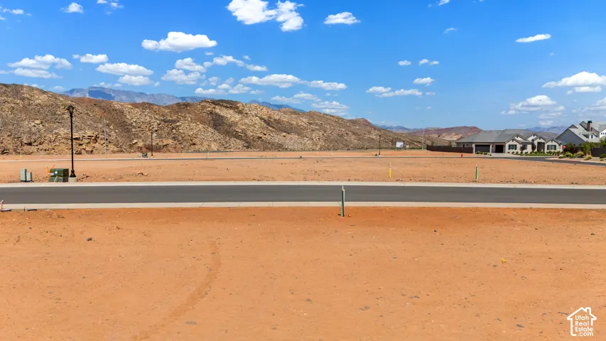 Expansive undeveloped lot featuring a paved road, mountain backdrop, and utility access points
