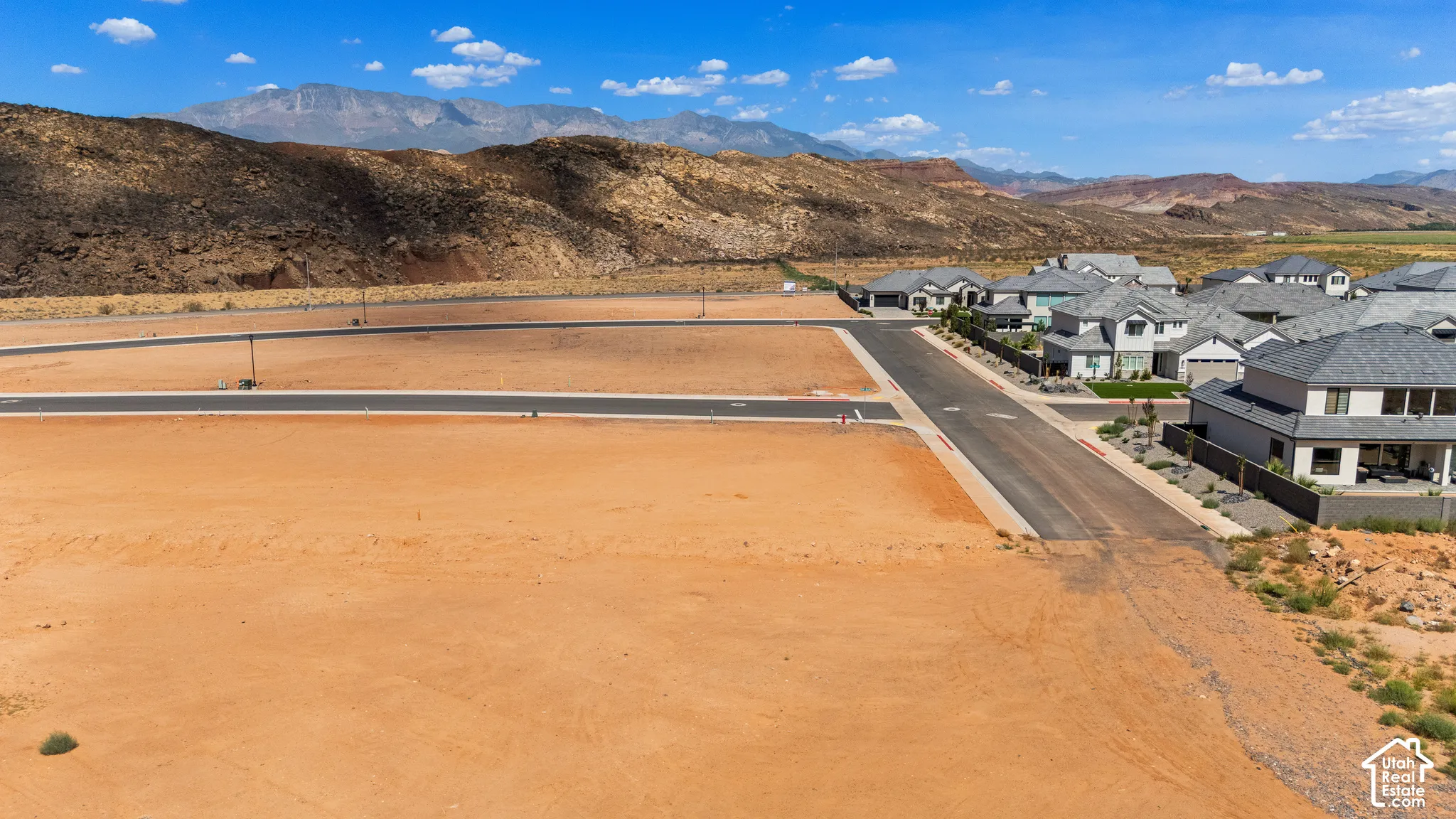 Graded lot with paved road infrastructure, surrounded by a developing residential area, and a mountain backdrop