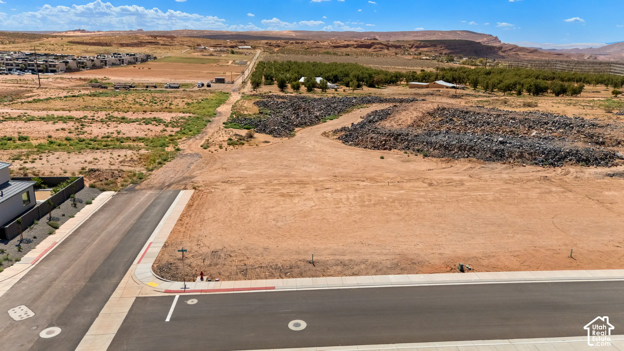Expansive land parcel with graded terrain, paved street frontage, and established infrastructure including sidewalks and curbs