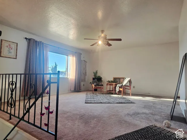 Open concept living space with carpeted flooring, a ceiling fan, and a large window