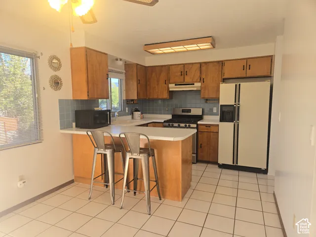 Kitchen featuring wood cabinetry, a gas range with a stainless steel hood, a tile backsplash, and a breakfast bar