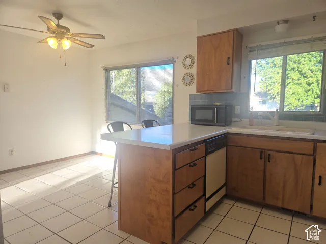 Kitchen featuring wood cabinetry, white countertops, tile flooring, a built-in dishwasher, and a ceiling fan with integrated lighting