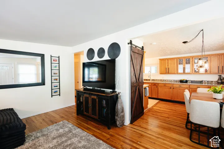 Hardwood flooring throughout, a dark wood-finish barn door, light wood-finish cabinetry, a white tile backsplash, and a modern ceiling light fixture