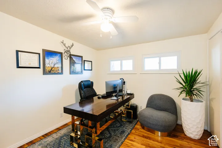 Wood-finish flooring with white baseboards, two horizontal windows, and a ceiling fan with integrated lighting