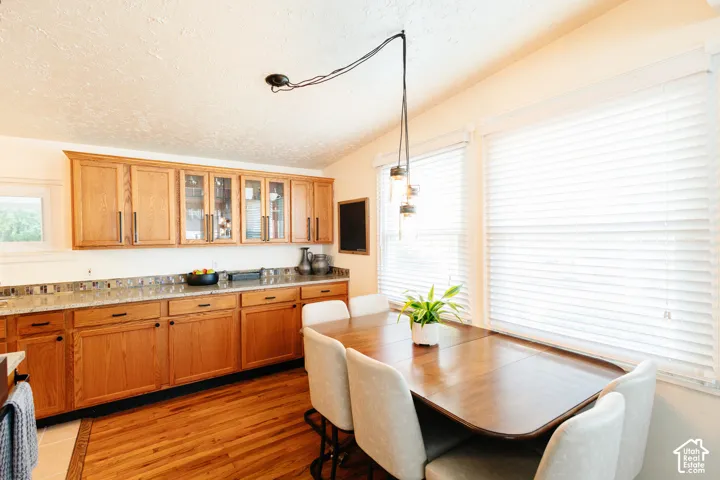 Wood-finish flooring with a tiled border, warm wood cabinetry with varied door styles, stone-look countertops, and a dining area with pendant lighting