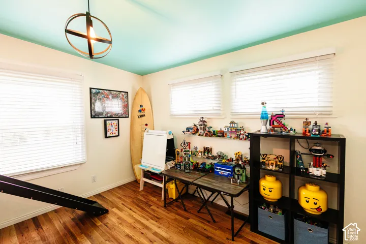 Wood-finish flooring, two large windows with blinds, a prominent ceiling light fixture, and a light blue ceiling