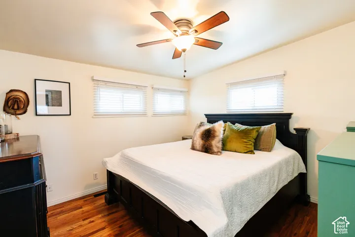 Hardwood flooring, painted walls, multiple windows with blinds, a ceiling fan with integrated lighting, and a dark wood-finish bed frame