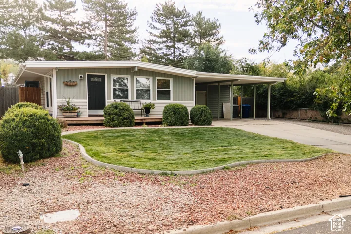 Exterior featuring a carport, front porch, mature landscaping, and a well-maintained lawn