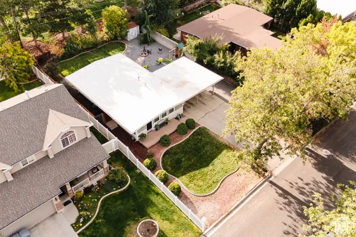 Expansive property featuring a white fence, mature trees, green lawn, and a paved driveway with a carport