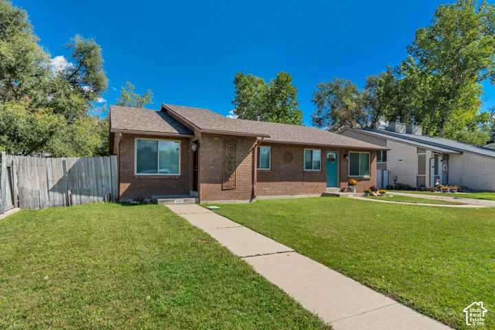 Brick exterior facade with a contrasting turquoise entry door, a concrete walkway, and a landscaped front yard with a wooden privacy fence