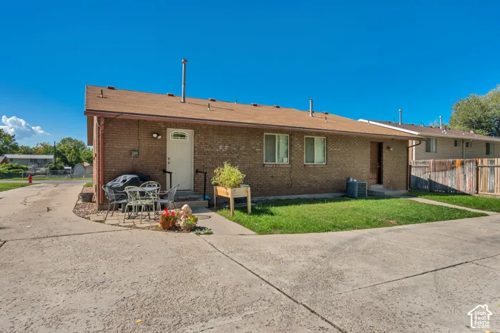 Brick exterior with a brown shingle roof, concrete patio, and a grass lawn