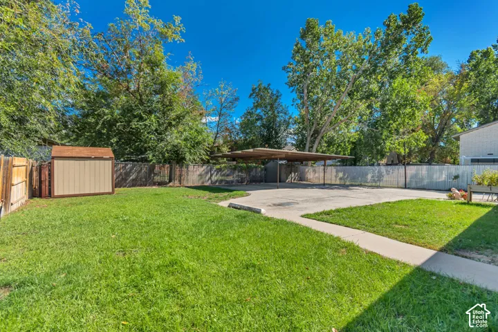 Manicured lawn, concrete pathway, fenced perimeter, storage shed, and a covered carport