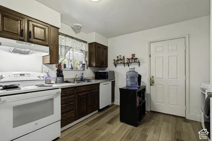 Wood-finish flooring, white appliances, dark wood-finish cabinetry, and a double basin sink