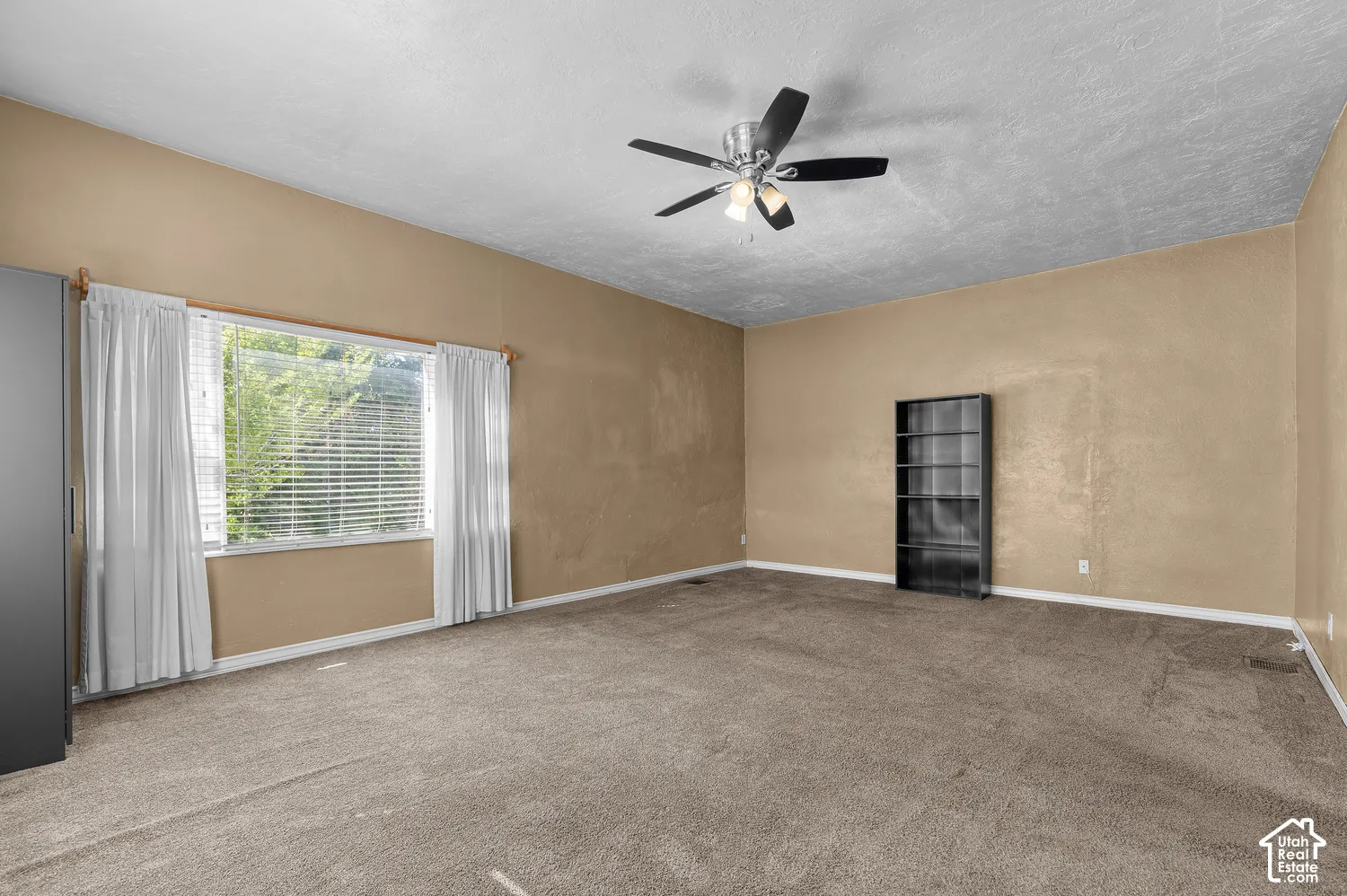 Vaulted ceiling with a ceiling fan light fixture, large window with blinds and curtains, and neutral-toned carpeting