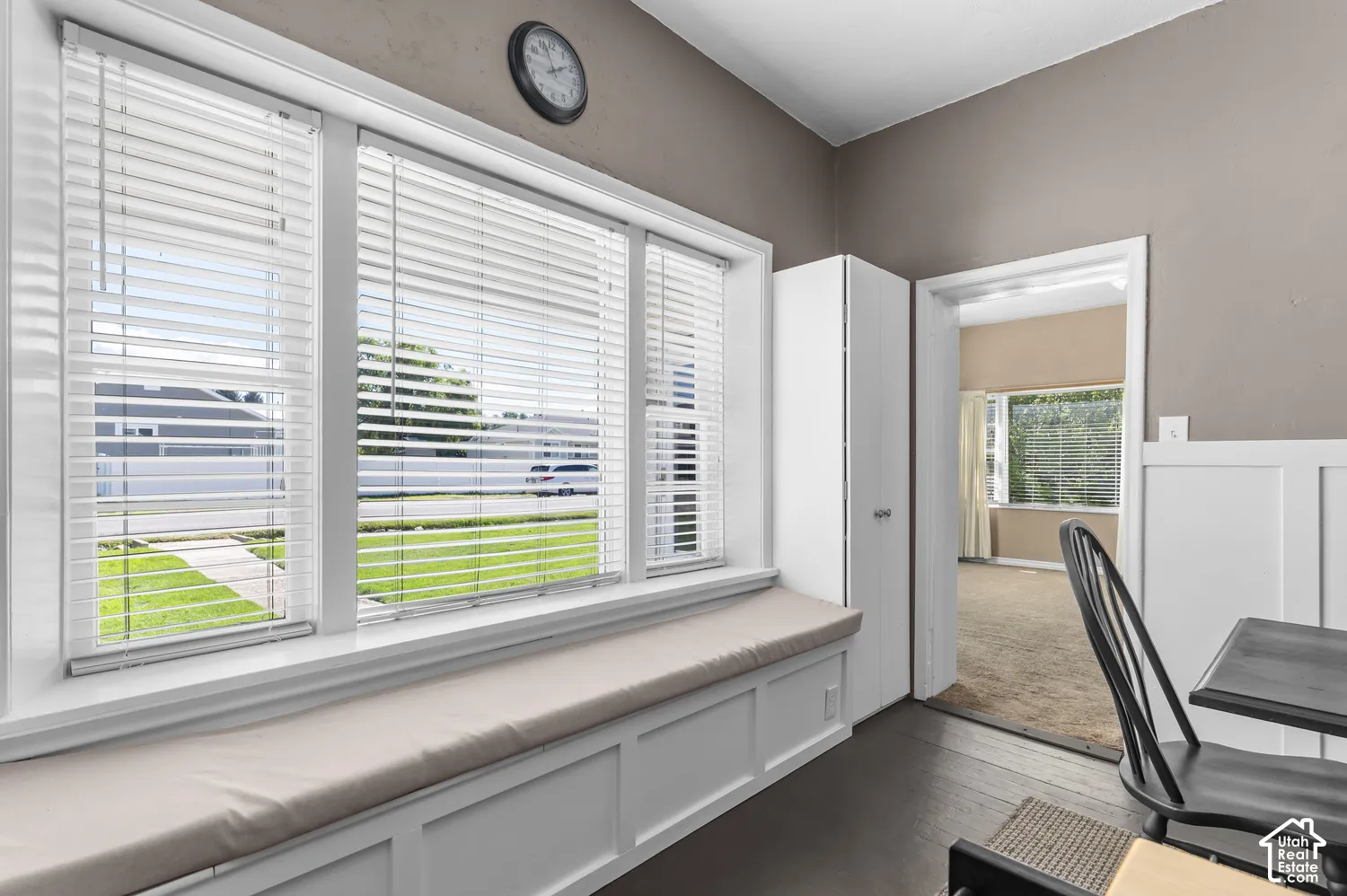 Built-in window bench with cushion, dark wood-finish flooring, and white paneled wainscoting