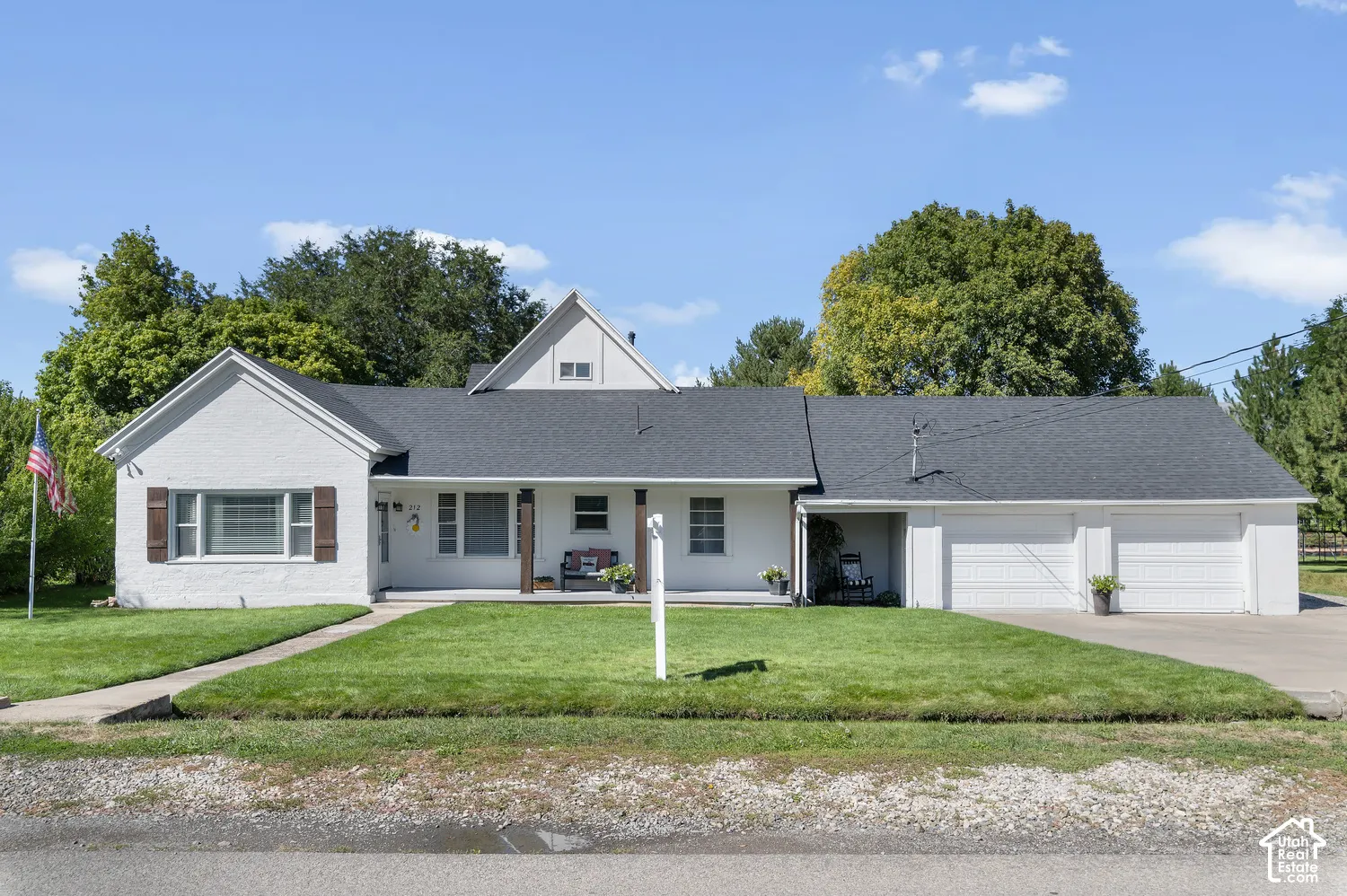 White stucco exterior with a dark shingle roof, covered front porch, and an attached two-car garage