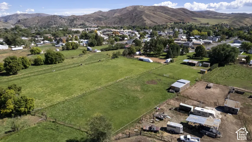Expansive green pastures with surrounding structures, bordered by a distant community and mountainous terrain