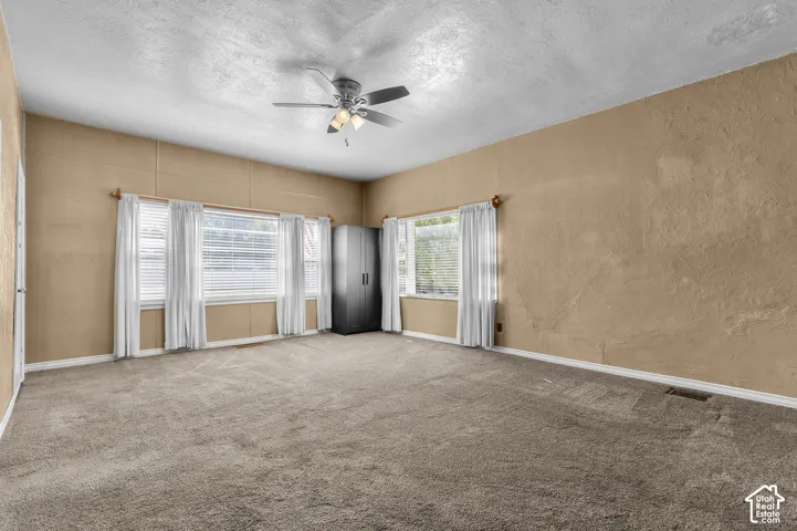Carpeted room featuring multiple windows, a ceiling fan with integrated lighting, and textured walls