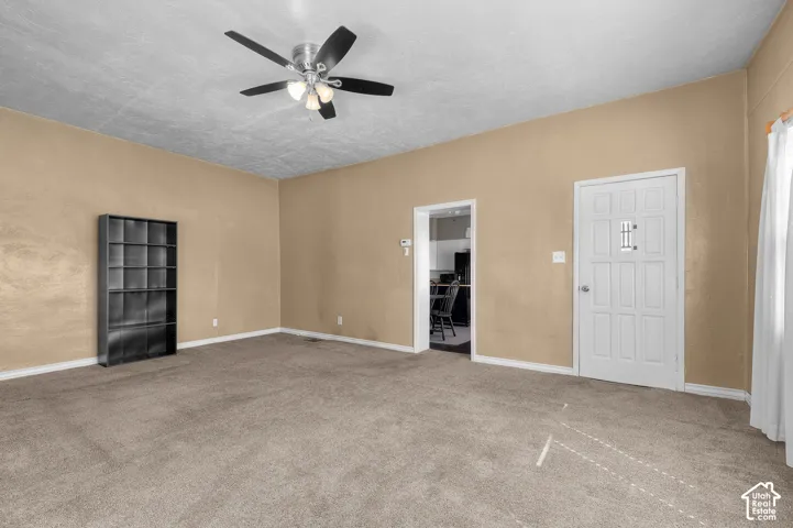 Carpeted living space featuring a ceiling fan with integrated lighting, a built-in shelving unit, and a white paneled door with decorative window inserts