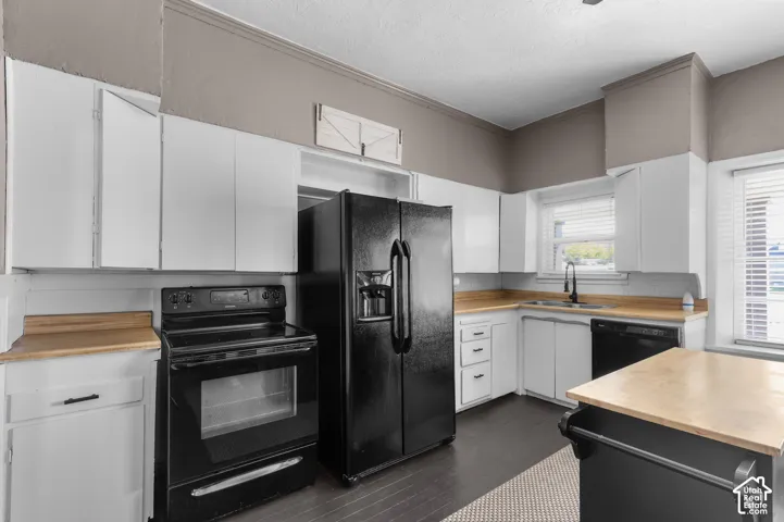 Kitchen featuring white cabinetry, light wood-finish countertops, black appliances, and dark wood-finish flooring