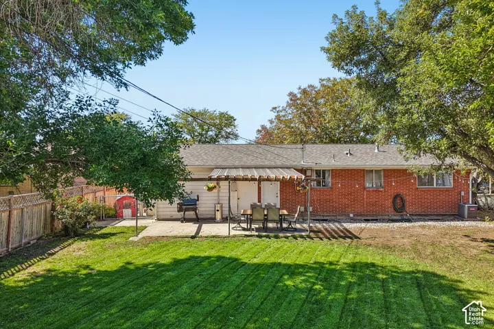 Expansive backyard featuring a manicured lawn, a stone patio with a pergola, and a brick exterior