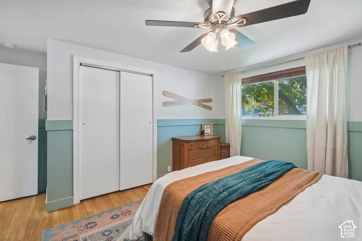Wood-finish flooring, ceiling fan with integrated lighting, sliding closet doors, and window with white trim