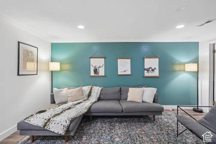 Recessed ceiling lighting, crown molding, wood-finish flooring, and a vibrant accent wall