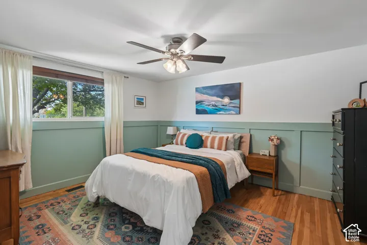 Hardwood flooring, picture window, ceiling fan with integrated lighting, two-tone walls with wainscoting, and recessed lighting