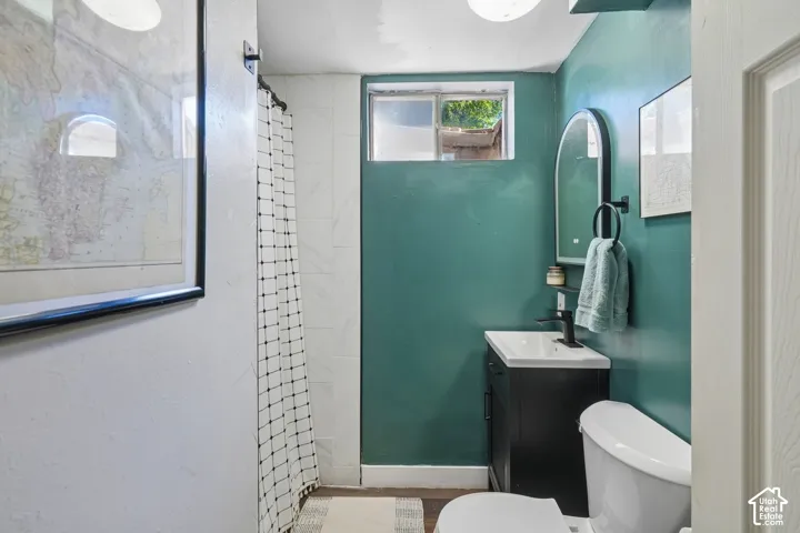 Bathroom featuring a vanity with integrated sink, wall-mounted mirror, toilet, and a tiled shower area
