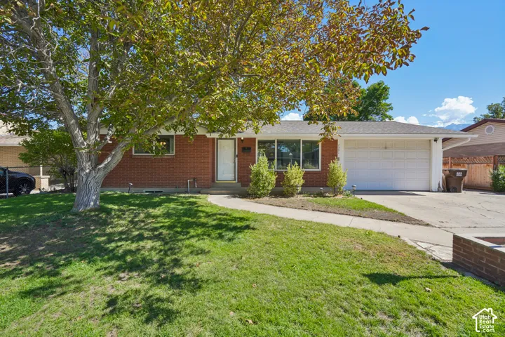 Brick exterior featuring a two-car garage, mature front yard tree, concrete pathway, and a well-maintained roof