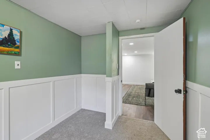 Wainscoting paneling with a painted finish, textured ceiling, light green wall paint, and gray carpet flooring