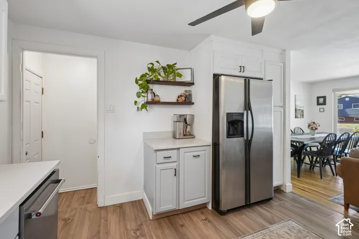 Stainless steel refrigerator, white cabinetry, wood-finish flooring, light-colored countertops, and open shelving
