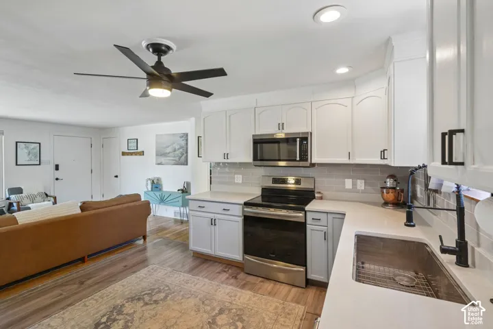 Kitchen features white cabinetry, stainless steel appliances, a tile backsplash, light-toned countertops, and a stainless steel sink with a black faucet
