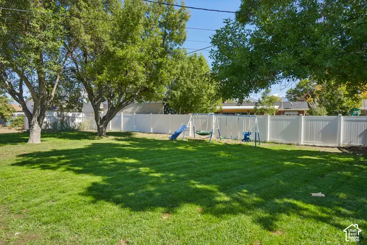 Expansive backyard featuring a manicured lawn, mature trees, and a white panel fence