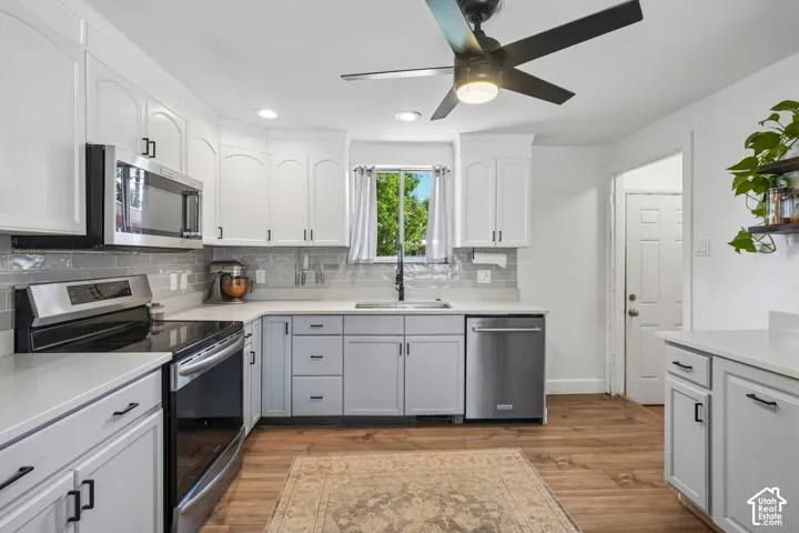 Modern kitchen featuring white upper cabinetry, gray lower cabinetry, stainless steel appliances, light countertops, and a gray tile backsplash
