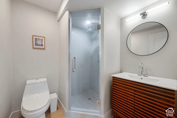 Enclosed glass shower with a rain shower head, wood-finish vanity with a white countertop, and an oval mirror with a black frame