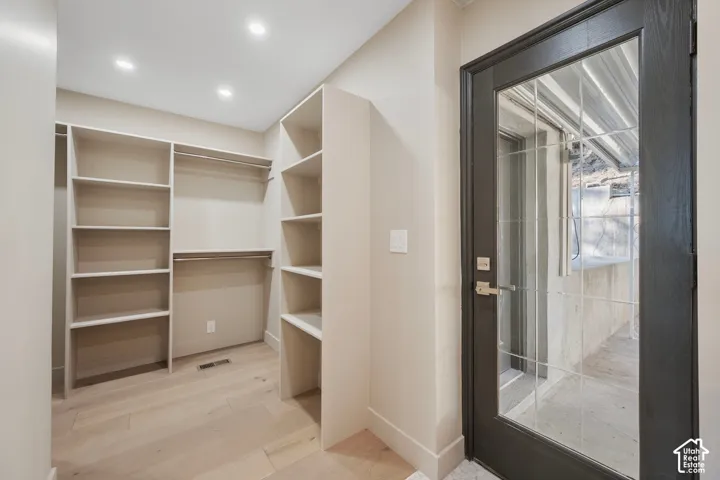 Walk-in closet with built-in shelving, hanging rods, recessed lighting, and light wood-finish flooring