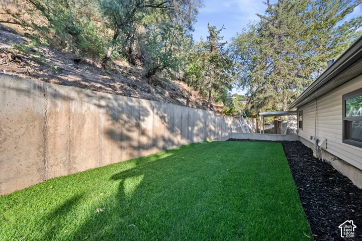 Expansive artificial turf area, concrete retaining wall, dark mulch landscaping, mature trees, and vinyl siding exterior