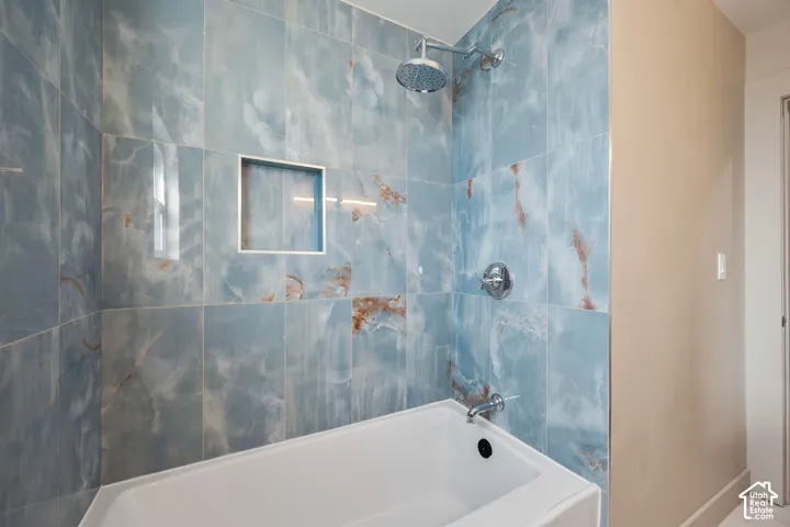 Bathtub with a tiled surround, integrated shower niche, rainfall showerhead, and polished chrome fixtures