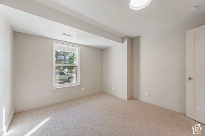 Recessed ceiling light, neutral wall color, single window with white trim, light-toned carpeting, and a white door with a chrome knob