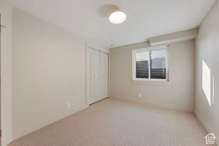 Neutral-toned carpeting, white walls, double bi-fold closet doors, and a window with blinds