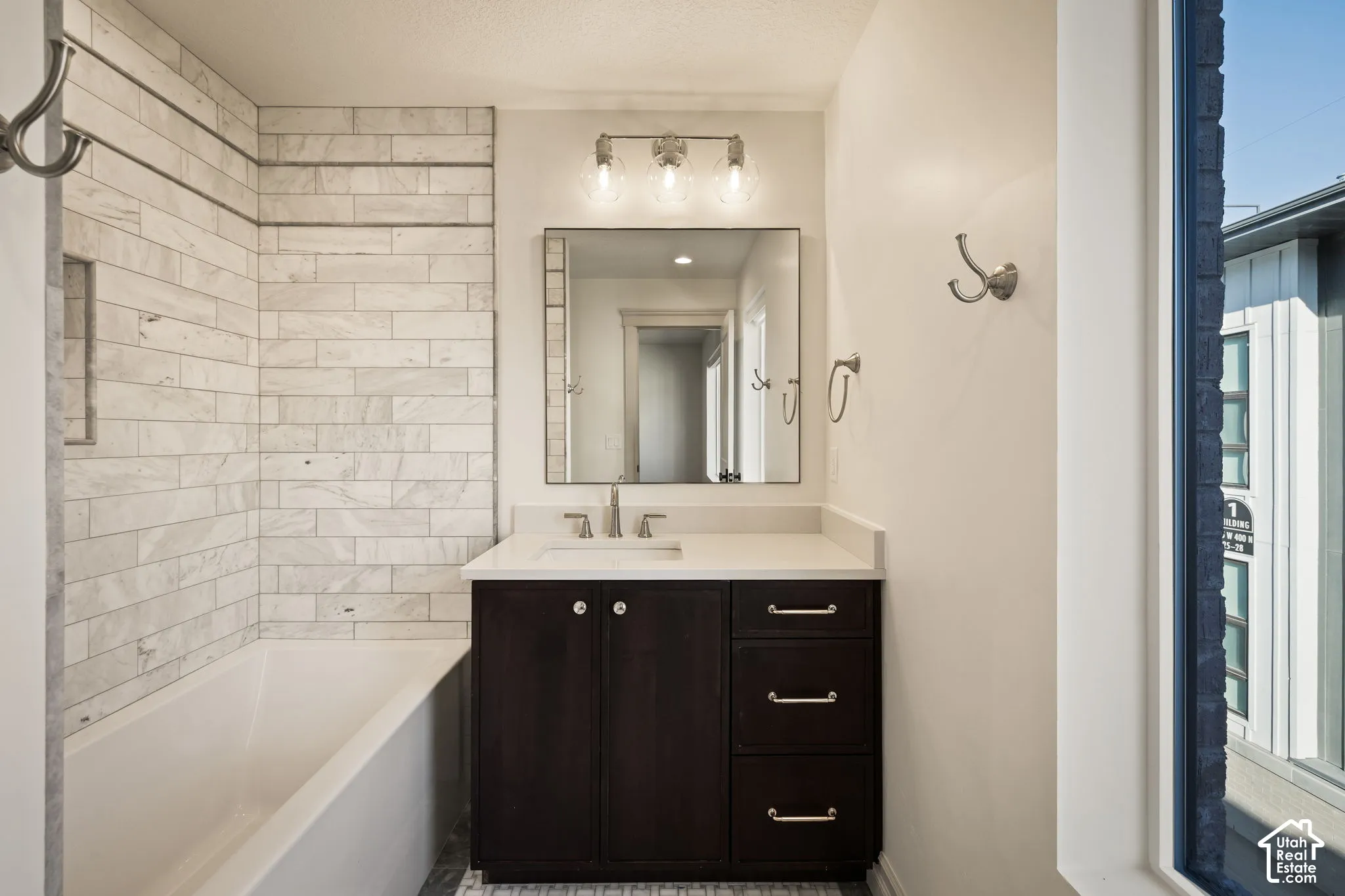 Bathroom featuring a white subway tile surround, dark wood-finish vanity, light-toned countertop, and mosaic tile flooring