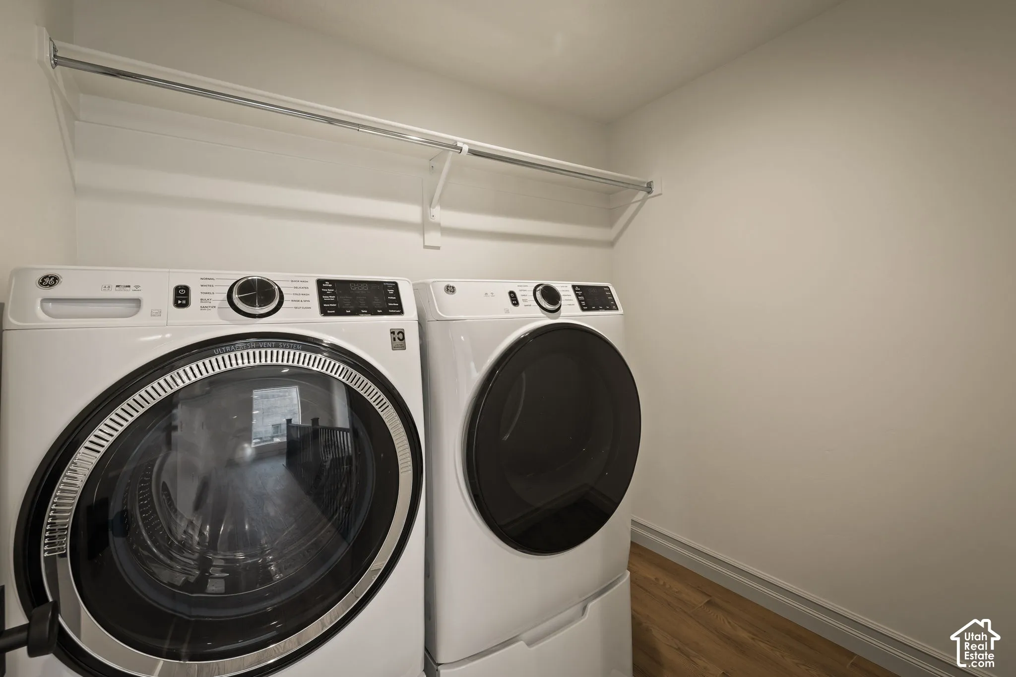 Integrated laundry area featuring wood-finish flooring and a white storage shelf with a hanging rod
