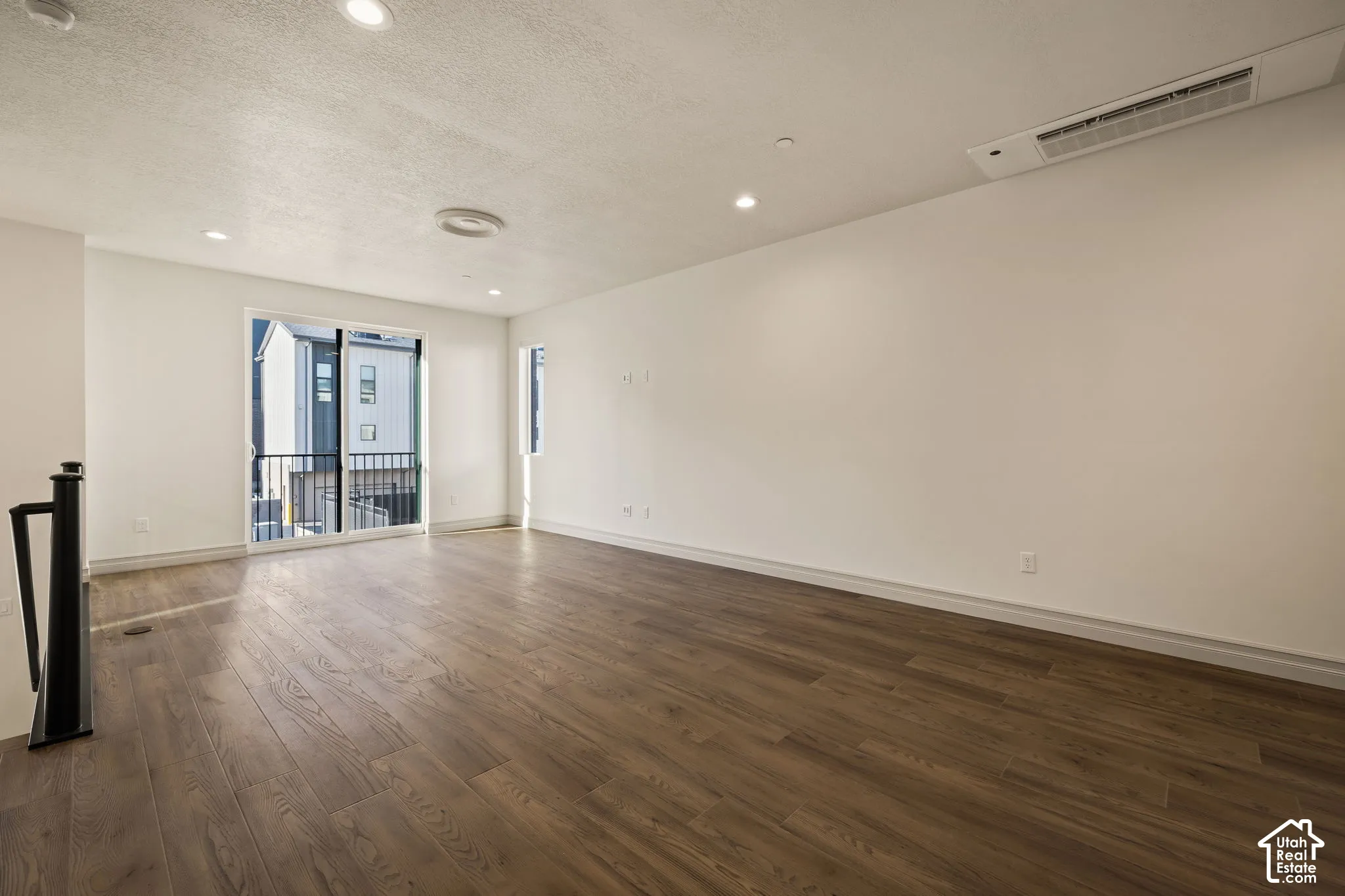 Spacious room featuring wood-finish flooring, recessed lighting, and a sliding glass door leading to a balcony with black metal railings