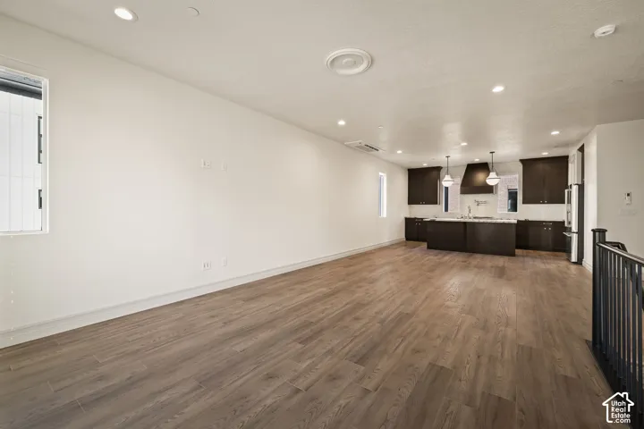 Recessed ceiling lighting, wood-finish flooring, dark wood cabinetry, stainless steel appliances, and a kitchen island with pendant lighting