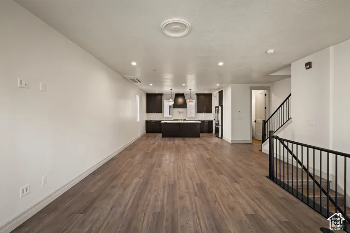 Open concept living area with wood-finish flooring, dark wood cabinetry, a central island, and a black metal staircase railing
