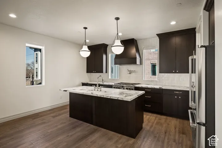 Kitchen featuring dark wood-finish cabinetry, light-toned stone countertops, a tile backsplash, stainless steel appliances, and wood-finish flooring
